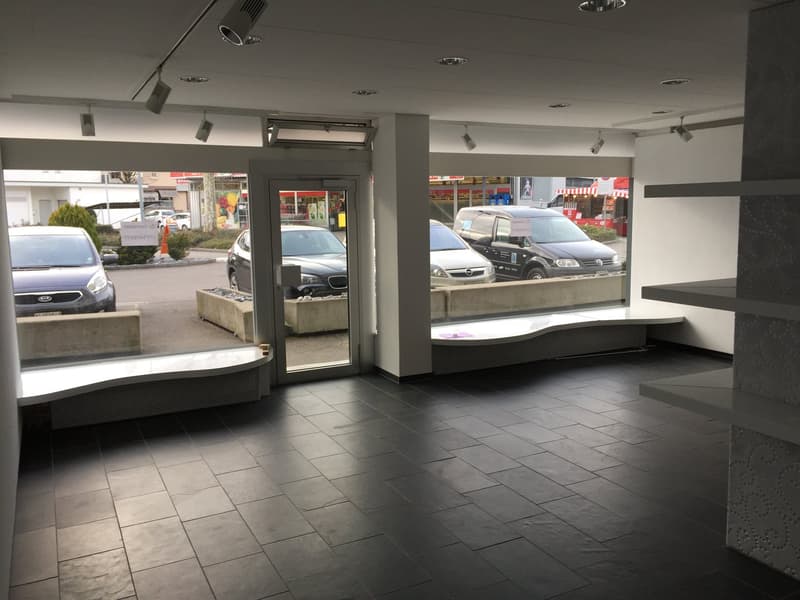 Empty interior with black tiles, large windows, glass doors, visible cars parked outside