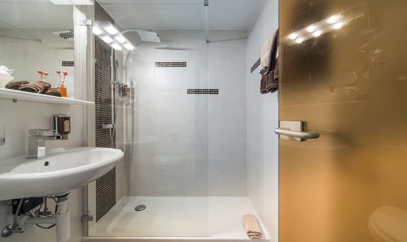 Modern bathroom with white tiles, walk-in shower, vanity sink, and private washing machine