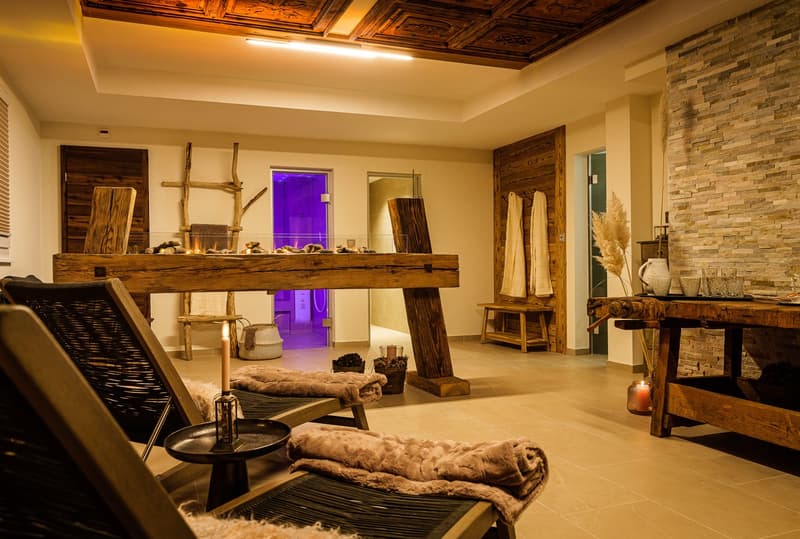Rustic living room with wooden ceiling, stone walls, wooden furniture, fur rugs, and a fireplace