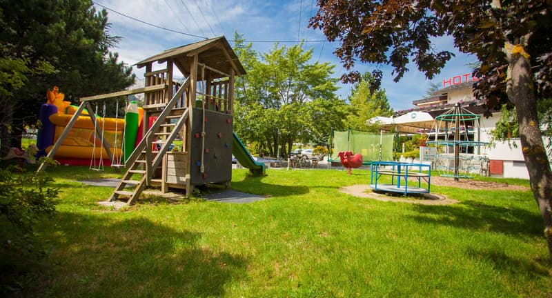 The image shows a well-maintained outdoor recreational area with a playground structure, including slides and climbing equipment, surrounded by lush greenery and trees. There is also an outdoor seating area with tables and chairs, suggesting this is a pub