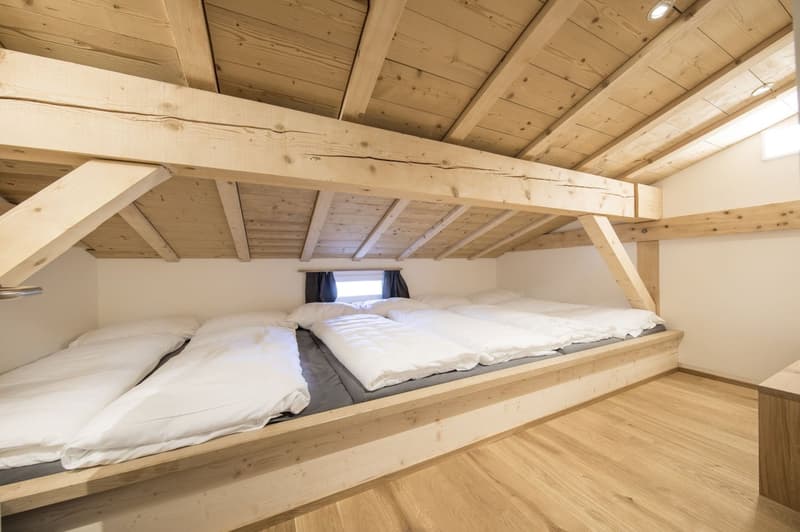 Cozy attic bedroom with wooden beams and ceiling, wooden floor, and a large bed with white bedding.