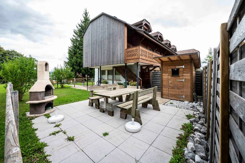 Patio with dining table, bench, woodshed, raised ground floor, grill, wooden fencing, grass, trees