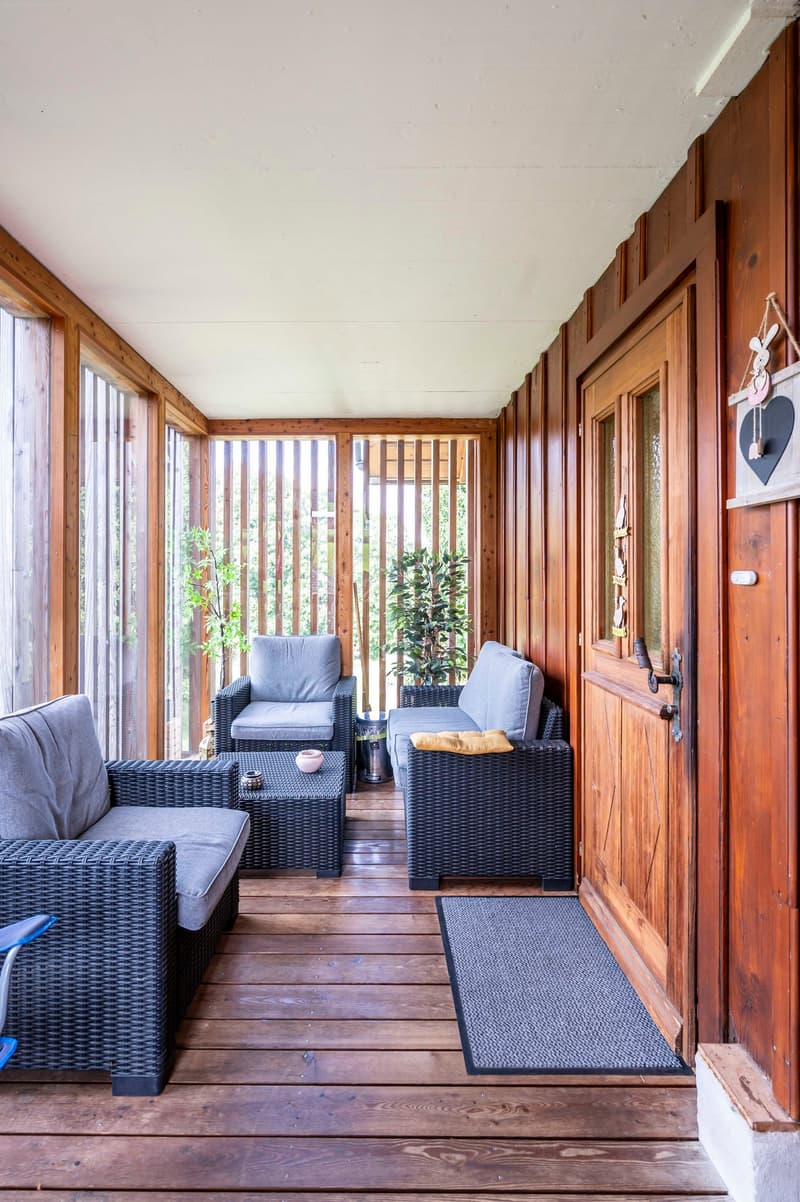 wooden deck, gray wicker sofa, wooden walls, glass windows, wooden door, mat, indoor plants