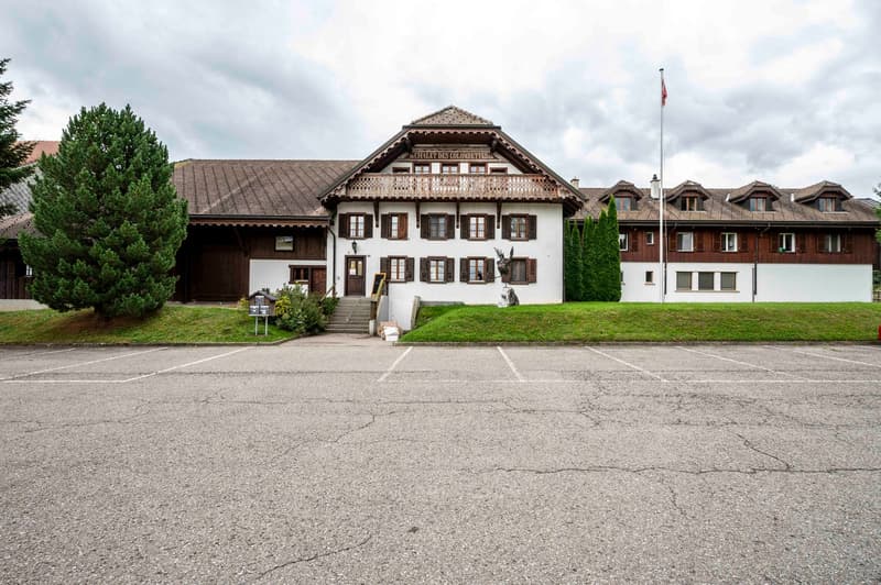 large 2-story house, wooden balconies, many windows, multiple trees, parking lot