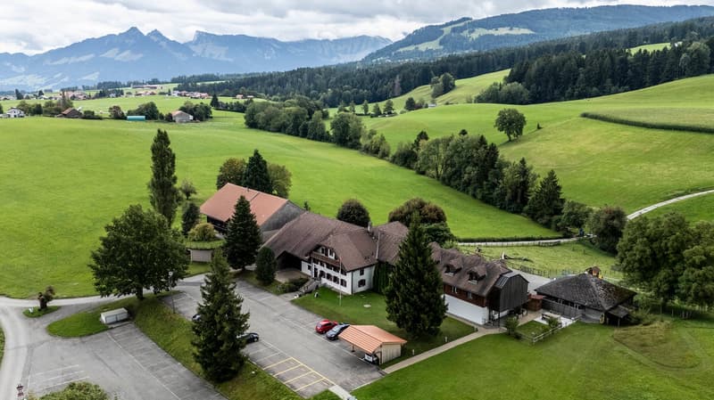 aerial view, 3 buildings, brown roof, green valley, parking lot, mountains