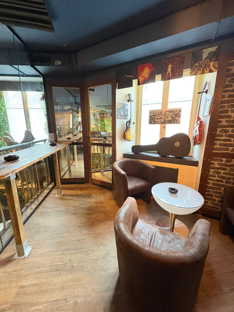 small room, wooden floor, wall-mounted guitars, glass walls, leather chairs, center table