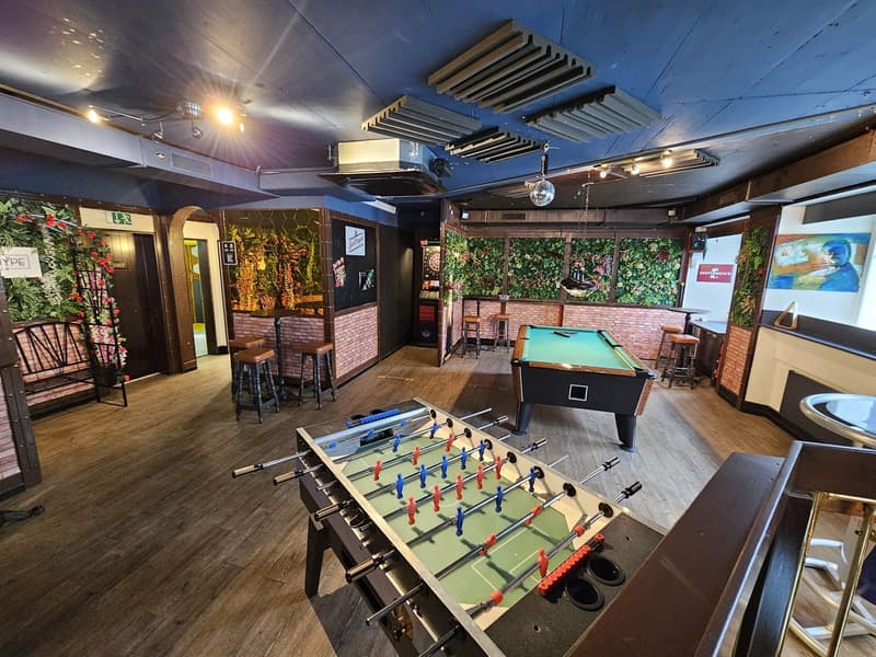 Two foosballs, a pool table, barstools, a bench, and a brick wall with a mural.