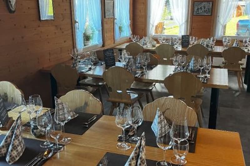 a dining area with tables and chairs, wooden walls, white curtains, wine glasses, and plates on the tables