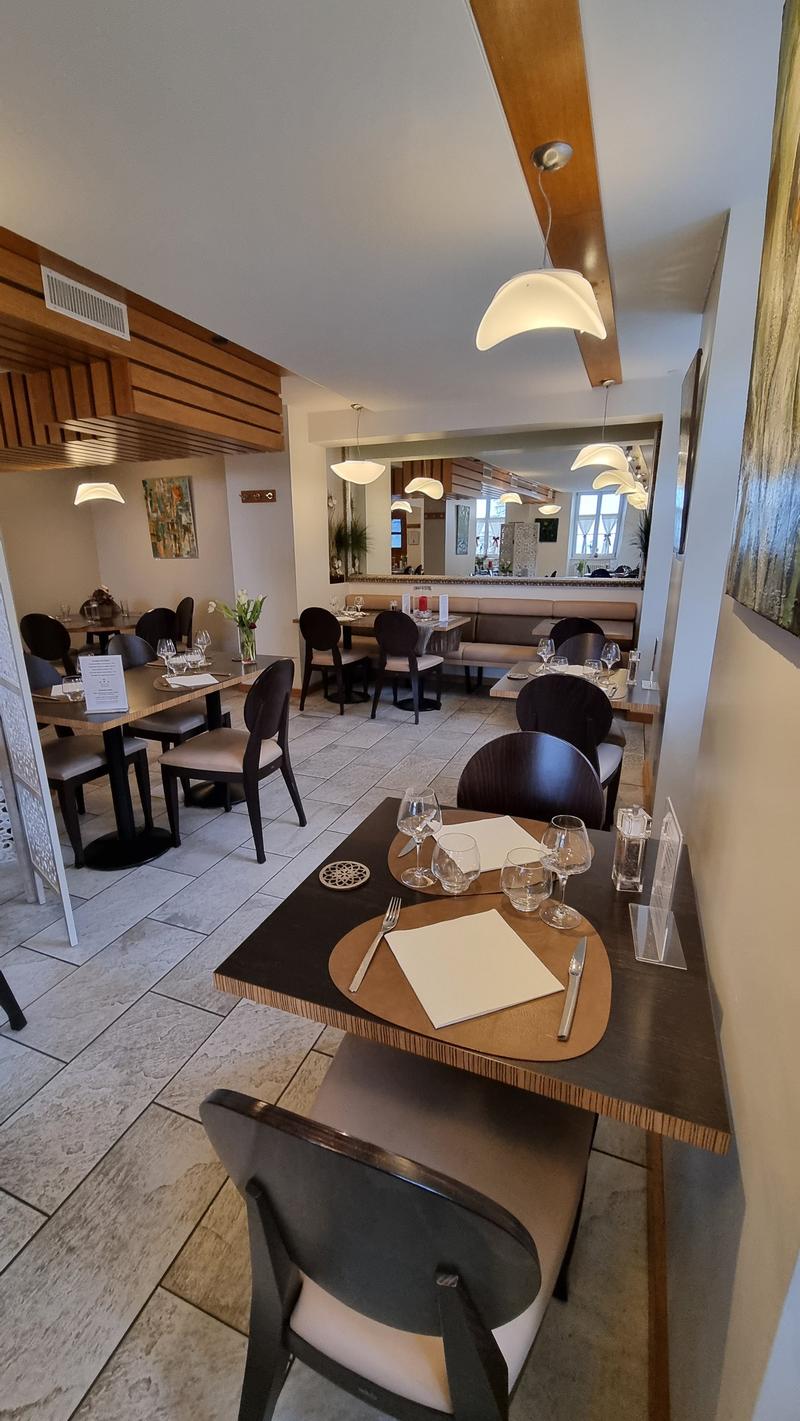 A restaurant with wooden tables and chairs, a large mirror on the wall, and a wooden ceiling with hanging lamps.