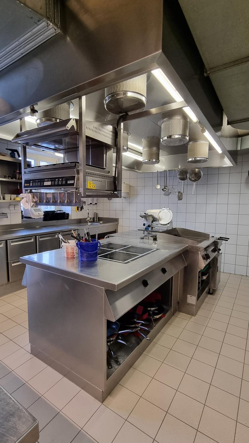 Stainless steel countertops, gas stove, oven, sink, cabinets, tiled floor, hanging pots and pans, exhaust hood, microwave, refrigerator, and other kitchen appliances.