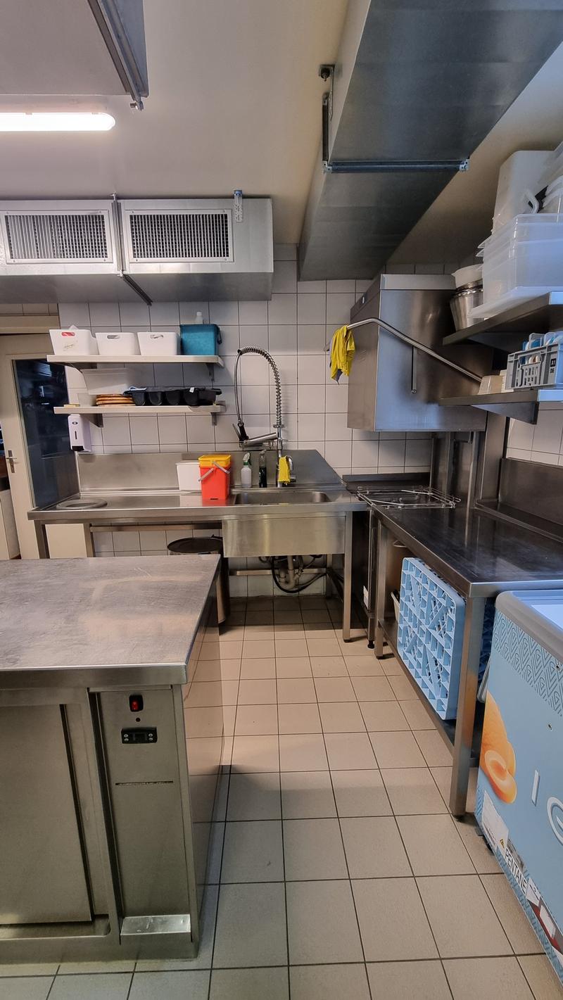 Commercial kitchen with stainless steel countertops, sink, shelves, and appliances.
