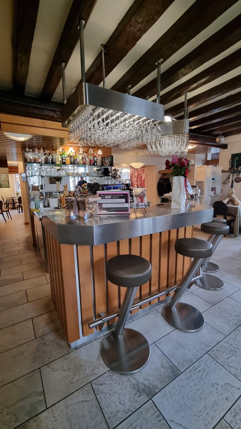 A bar counter with stools, a flower vase, a wine glass rack, and shelves with bottles and glasses.
