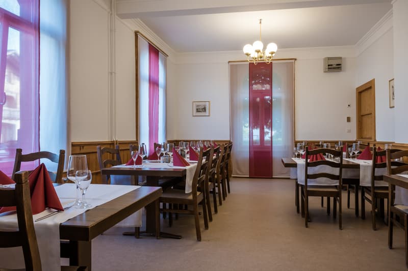 Dining room with wooden tables and chairs, white tablecloths, red napkins, wine glasses, and a chandelier
