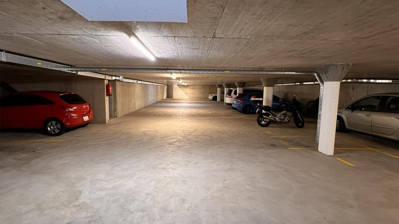 Underground parking space with parked cars and motorcycles.