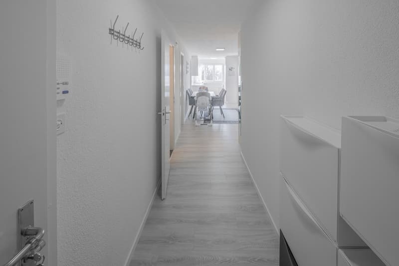 white walls, wooden floor, open door, hallway leading to dining area with table and chairs