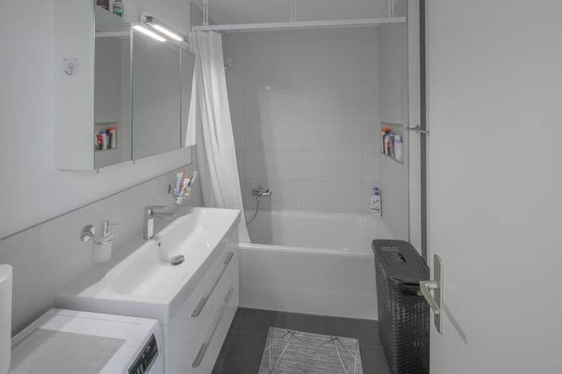 white tiles, white bathtub, white sink, white cabinets, white toilet, white shower curtain, white floor
