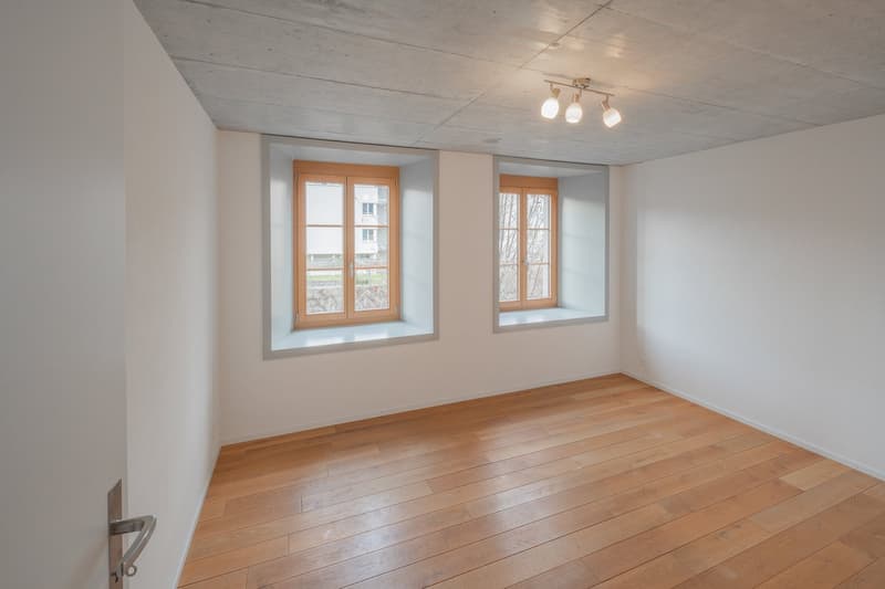Empty room with wooden floor and white walls. Two windows with wooden frames and sills.