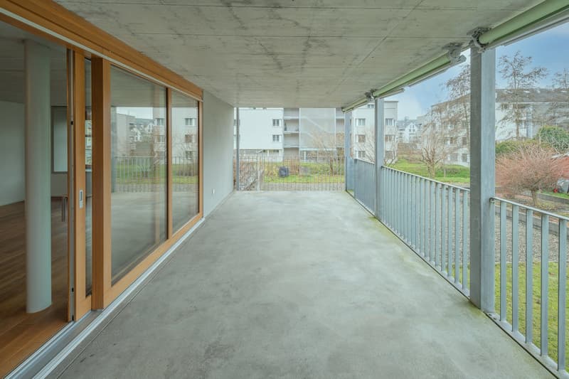 Empty terrace, wooden floor, metal railings, tall buildings in the background.