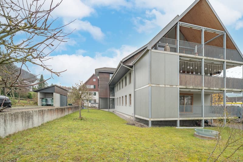 Modern apartment building, gray exterior, multiple balconies, garage attached, green lawn in front