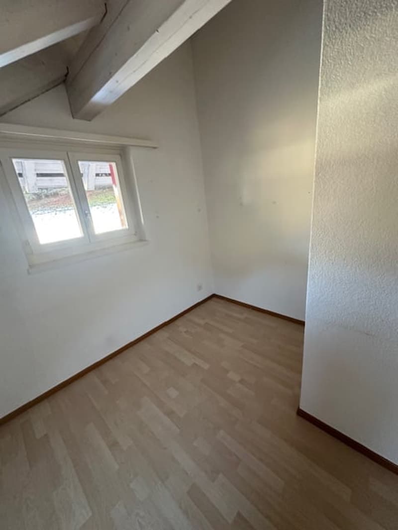 Empty room with wooden floor, white walls, white ceiling beams, small window