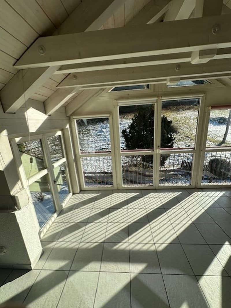 sunny room with tile floor, white wooden beams, 4 large windows, balcony with railings