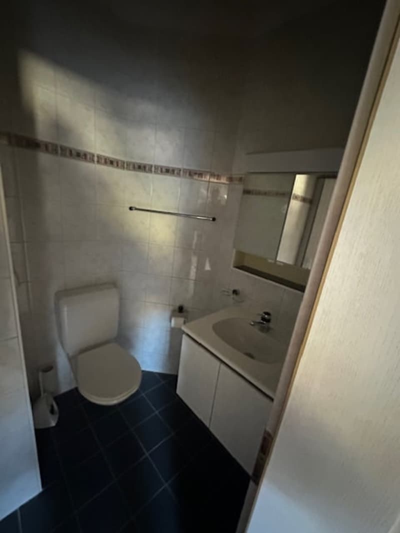 Small bathroom with tile flooring, white sink, mirror, toilet, and cabinet