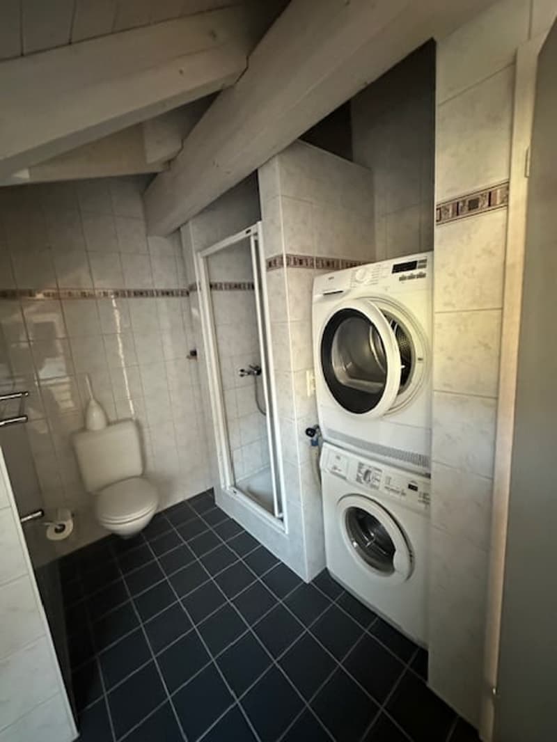 Laundry room with tiled walls, tiled floor, white appliances, glass door shower, toilet