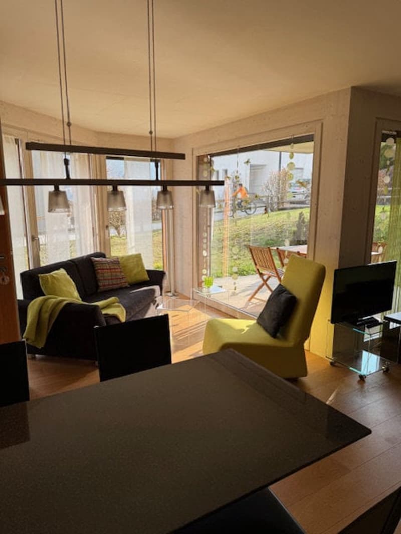 Living room with a couch, a yellow chair, a table, a television, and a glass door leading to a patio with outdoor furniture