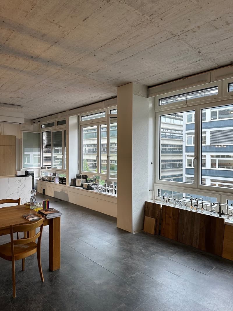Contemporary room with open design, dark flooring, wooden furniture, multiple windows, view of another building. Window sills with various objects. Wooden cabinets near the wall.