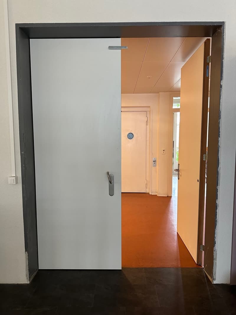 Two doors with a large hallway inside, tile flooring and white walls