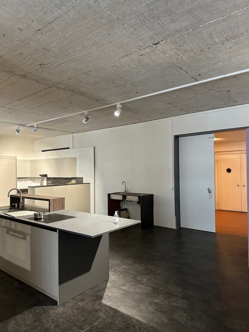 Modern kitchen with a large central island, undermount sinks, built-in faucets, sleek countertops, stainless steel backsplash, white cabinetry, integrated lighting, open shelves, and a small black appliance island with sink and faucet. A door leads to an