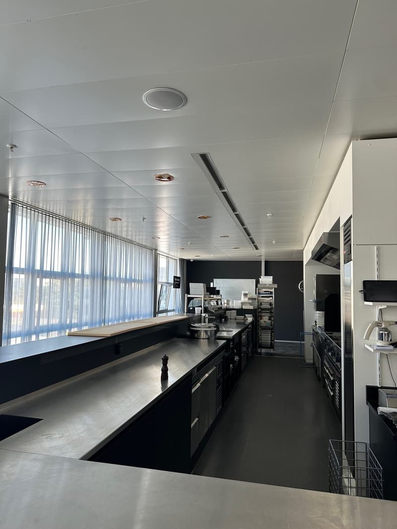 Empty kitchen with long countertop, various appliances, windows, and ceiling design.