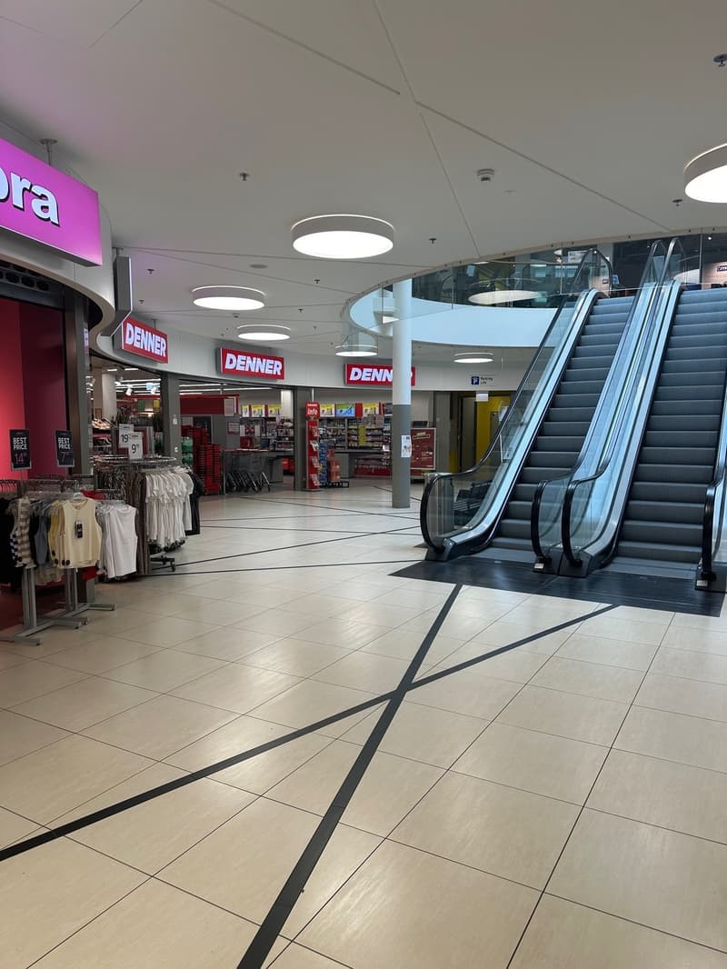 Empty mall with escalators, clothing store, and signage