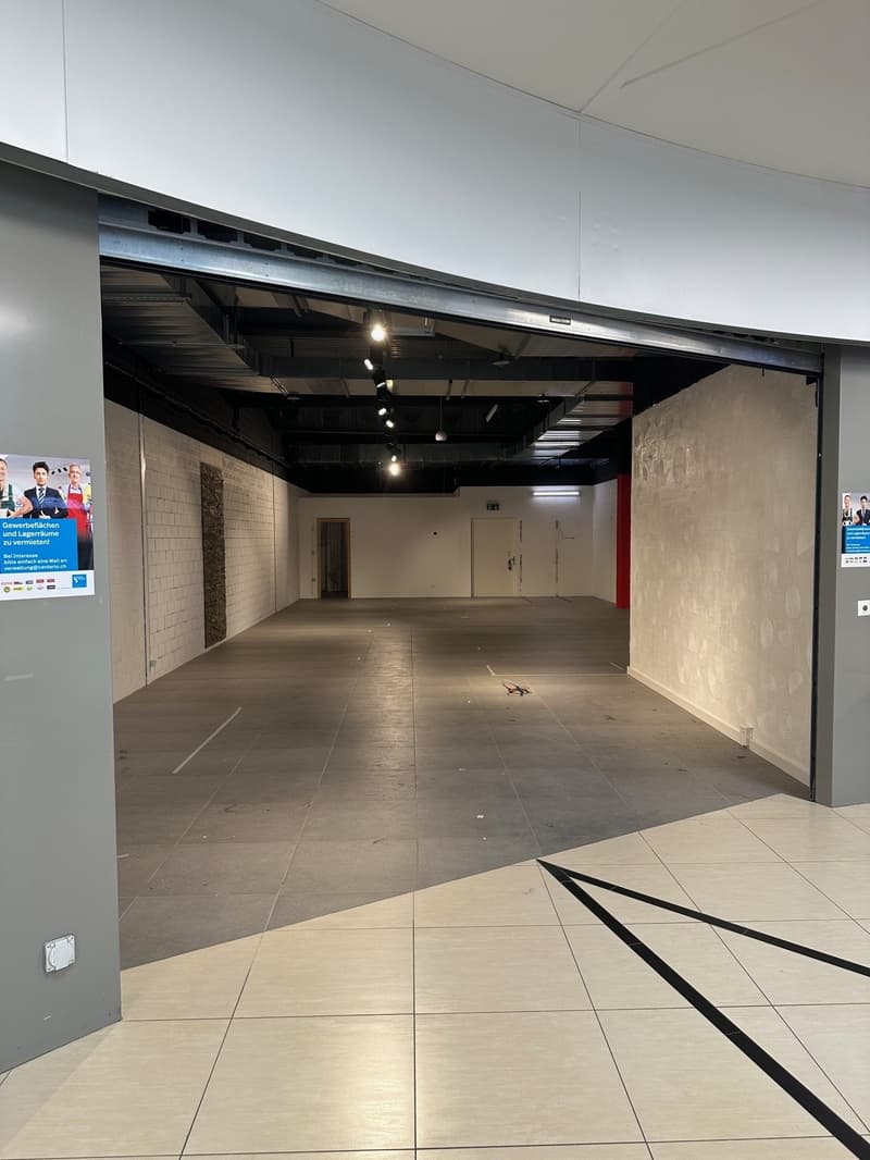 Empty room, tiled floor, white walls, open door, ceiling lights, advertisement posters