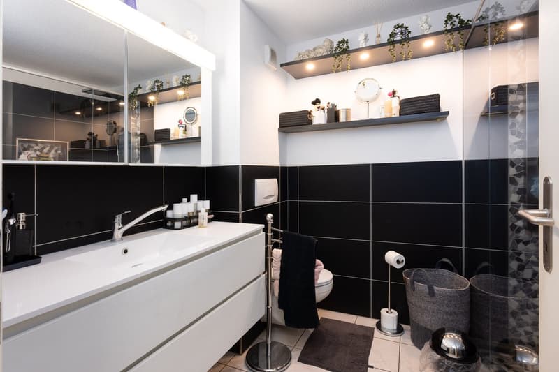 modern bathroom with black and white tiles, white vanity, mirror, shelves, toilet, and storage baskets