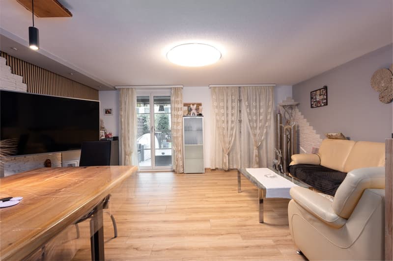 Living room with wooden floor, large flat screen TV, dining table, couch, coffee table, glass door, ceiling lights