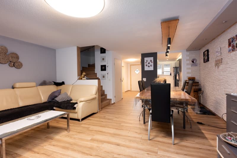 living room with wooden floor, beige sofa, dining table, wooden dining chairs, wooden coffee table, white walls, wooden staircase