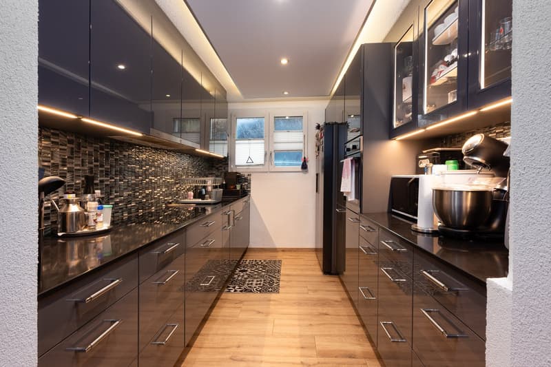 modern kitchen with black countertops, stainless steel appliances, wooden floor, cabinets, windows