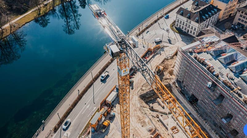 An aerial view of a bridge construction site over a river with a road, vehicles, machinery and construction materials.