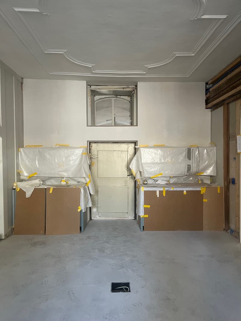 empty room, white walls, ceiling with moldings, two doors, two covered objects, floor covered with plastic