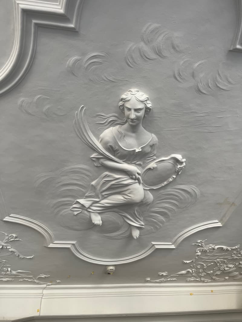 white ceiling with a female figure in relief, holding a mirror and a sword