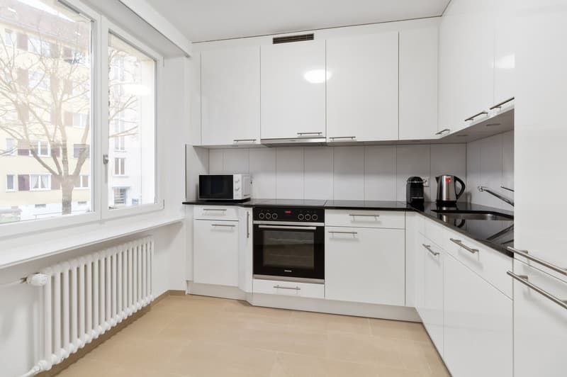 Spacious modern kitchen with white cabinets, black countertops, built-in oven and microwave, and a dishwasher. Large window providing natural light.