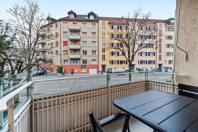 Multi-story apartment building with colorful facades, balconies, and a street view with trees and parked cars
