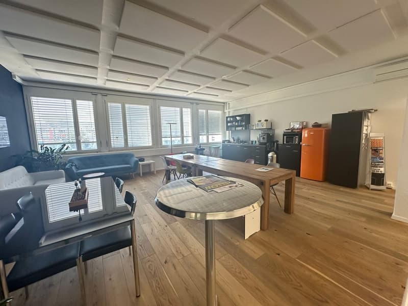 The image shows a spacious open-plan living area with a kitchen, dining, and living room. The space features hardwood floors, a coffered ceiling, large windows, and a mix of modern and rustic furnishings. The kitchen area includes a dishwasher and a priva