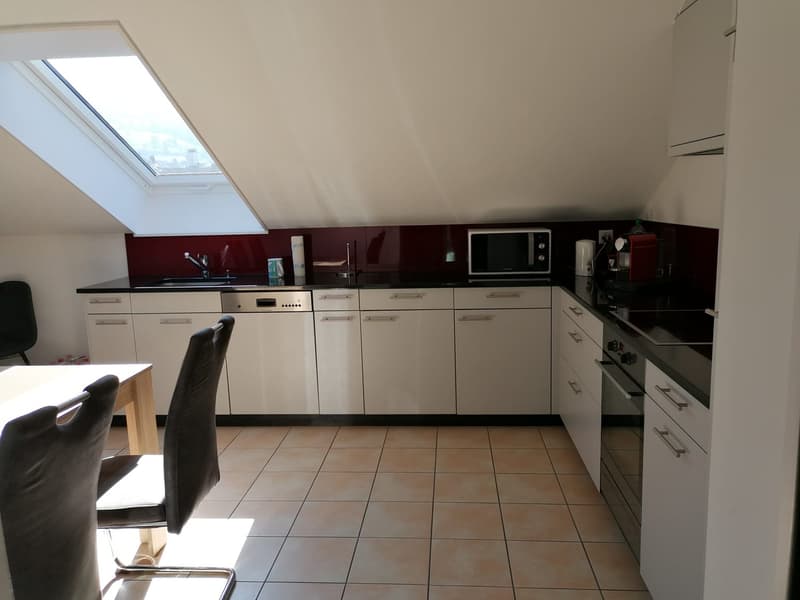 Spacious kitchen with white cabinets, black countertops, and tile flooring. Appliances including a microwave and dishwasher are visible. The kitchen has a window providing natural light.