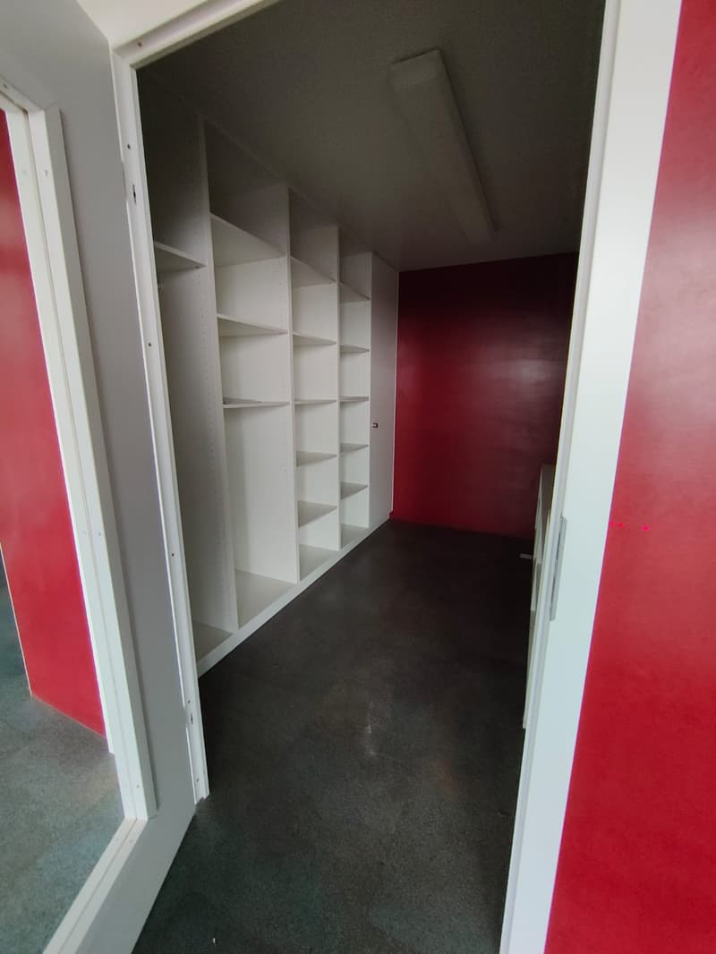 Empty room with tall shelves on one side and red walls.