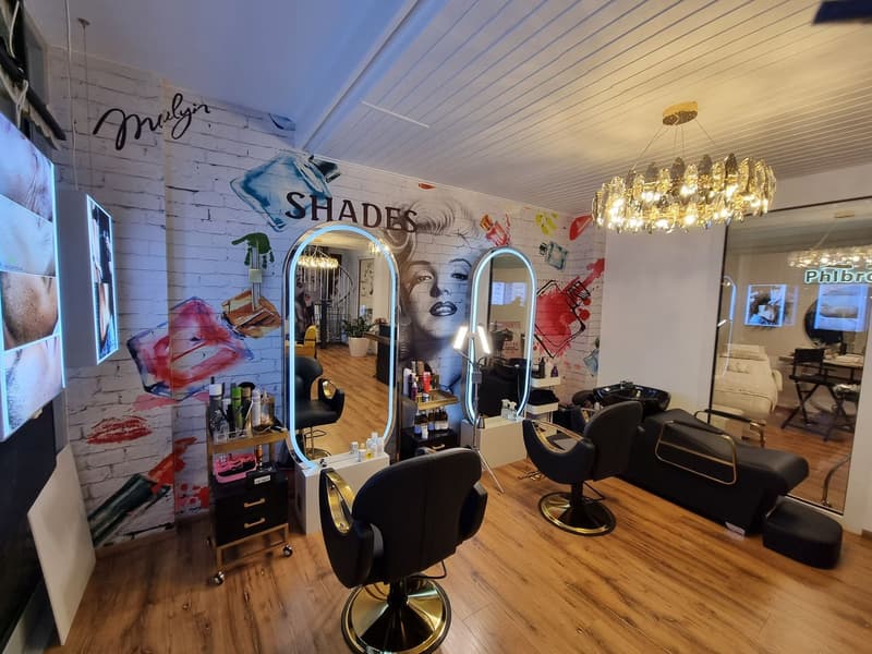 Beauty salon with wooden floors, brick walls, large mirrors, seating area, and a chandelier.