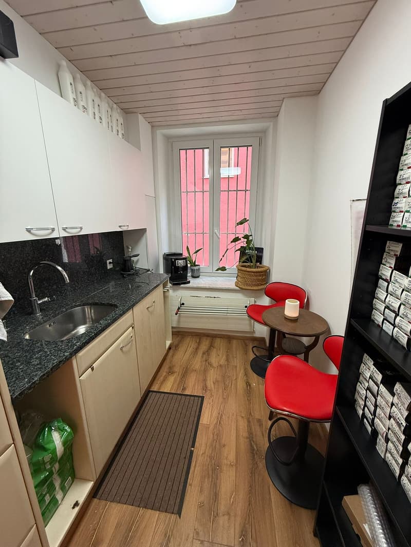 Compact kitchen with sink, countertop, small stove, window, coffee maker, seating area with table and chairs, cabinet and shelf