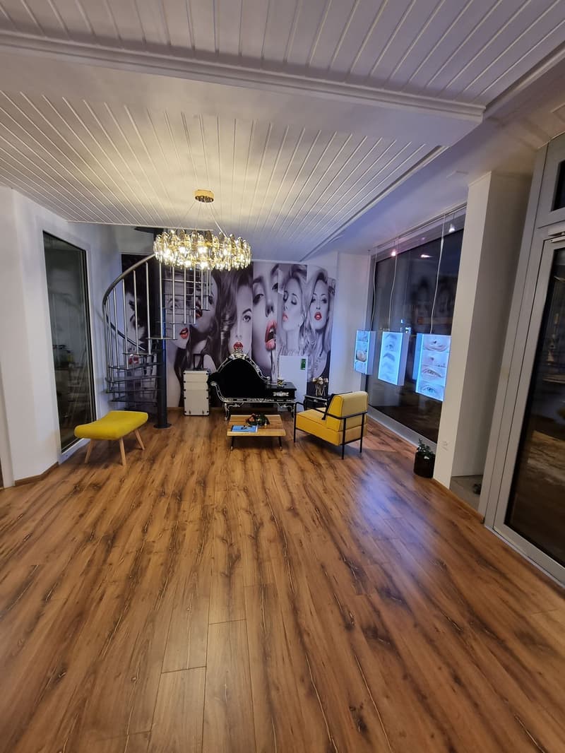 Hardwood floors, decorative chandelier, yellow armchair, black chaise lounge, glass windows, spiral staircase, white ceiling with wood texture, white wall.