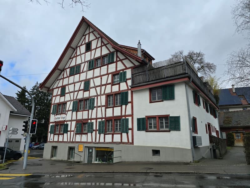 White painted, timber-framed house, red roof, multiple windows, red trims, small garden